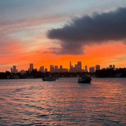 City skyline at sunset with boats on water and vibrant orange sky.